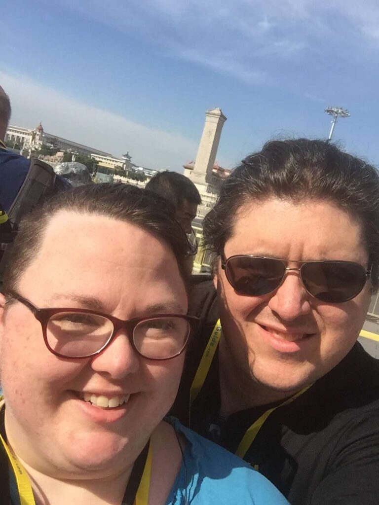 Janelle and her husband taking a selfie at Tiananmen Square in Beijing on a sunny day, both smiling, before the website security hack